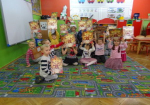 Dzieci oraz nauczycielka w czapce mikołajkowej z kalendarzami adwentowymi pozują do wspólnego zdjęcia.